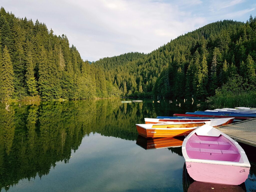 Colorful boats on a serene lake surrounded by pine forests in Romania, symbolizing the calm business climate and benefits of the Micro Company Regime for taxation in Romania.