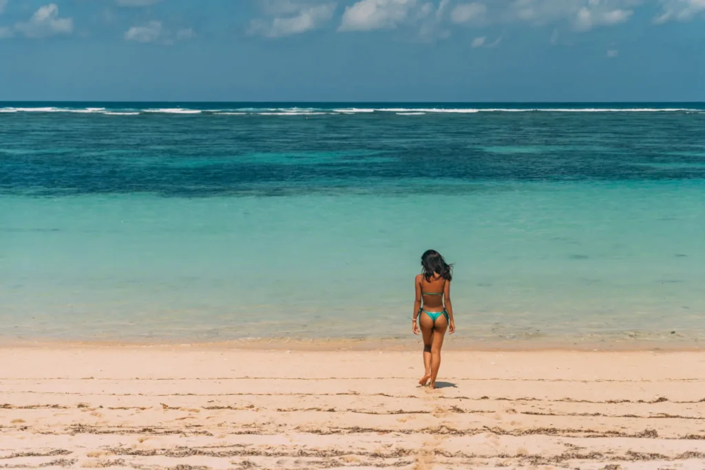 Woman walking along an empty Caribbean beach with clear turquoise water in Panama